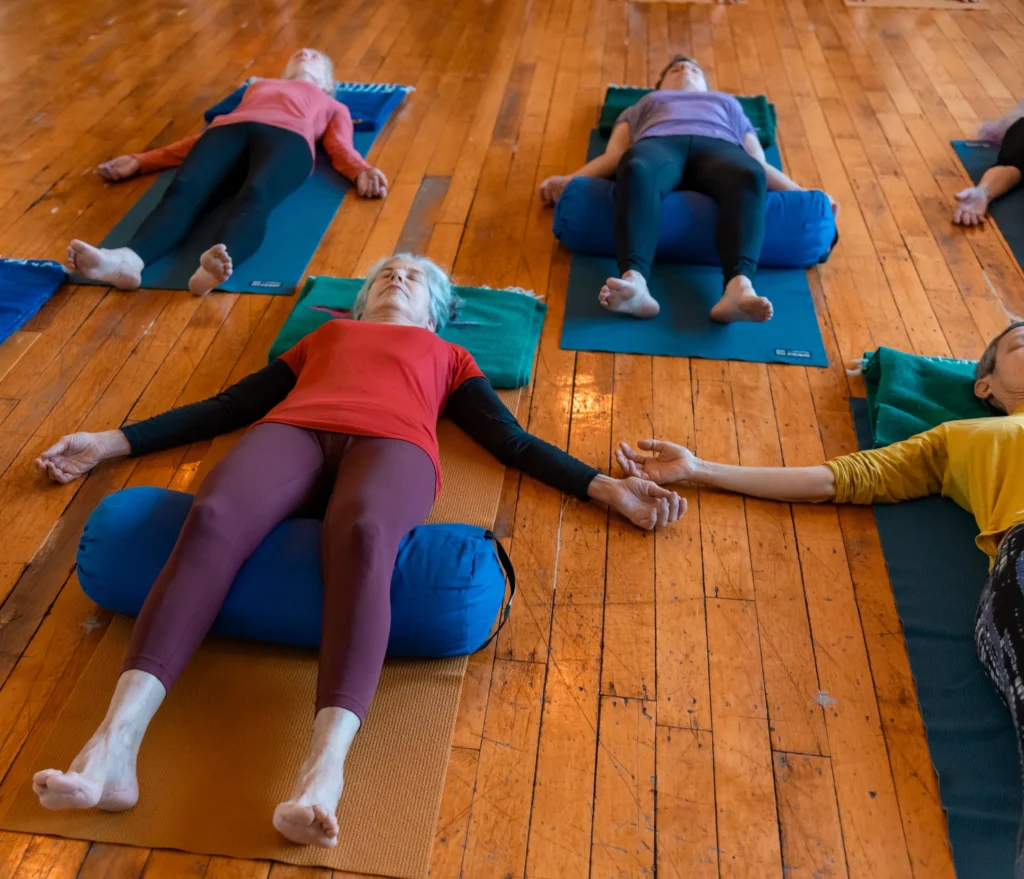 Students resting in supported Savasana on mats and bolsters in the yoga studio